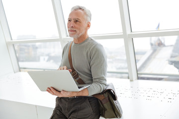 Photo of pleased gray-haired man holding and using laptop