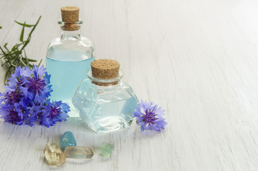 Obraz na płótnie Canvas Cornflower flower blue water in glass bottles and bath salt on white wooden table background. Essential oil of knapweed for aromatherapy or SPA salon