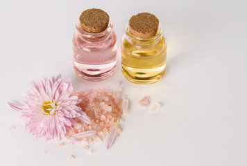 Fototapeta na wymiar Water flower or chrysanthemum essential oil in glass bottles with pink bath or SPA salt on white background