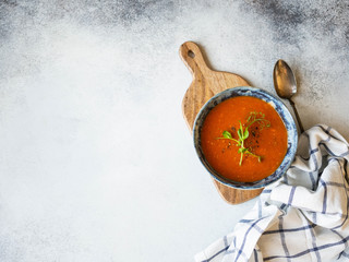 Fresh Tomato soup with spices and fresh pea sprouts in blue rustic bowl on wood board on light background. Copy space