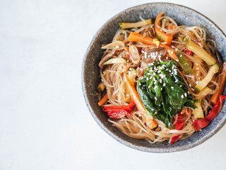 Blue bowl with rice noodles and various vegetables steer fry on a grey background.