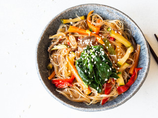 Blue bowl with rice noodles and various vegetables steer fry on a grey background. Top view