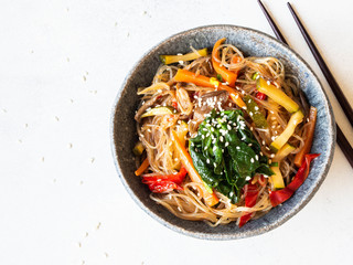 Blue bowl with rice noodles and various vegetables steer fry on a grey background.