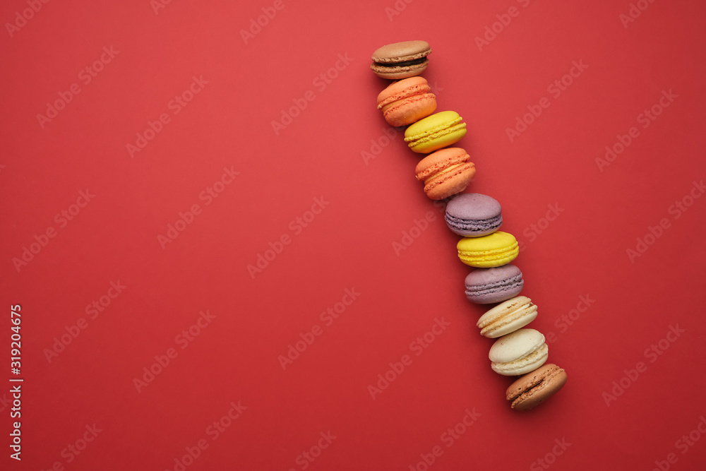 Poster round multi-colored baked macarons with cream lie in a line on a red background