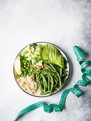 Quinoa bowl with green beans, green peas, cucumber, avocado, and pine nuts and measure tape for measuring body volumes on grey background. Healthy eating concept. top view