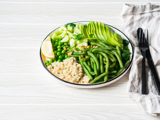 Quinoa bowl with green beans, green peas, cucumber, avocado, and pine nuts on white wood...