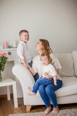 Beautiful young mother, little son, little daughter are sitting on the sofa at home. Mothers Day. A happy family. Cozy.