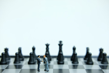 Miniature business concept - two businessman make handshake agreement in front of chess pawn