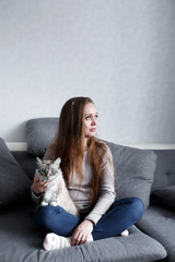 Young trendy woman sitting on the couch at home with domestic cat