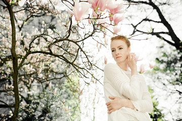 Portrait of charismatic woman standing under the blossom magnolia tree