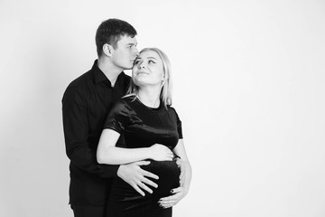 Pregnant woman and her husband hugging and holding onto your stomach in black clothes on a white background. Black and white picture. Beautiful married couple. Copy, empty space for text