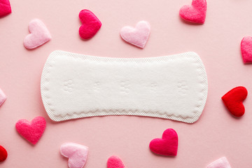 white menstruation pad with red hearts as blood drops on rose background, women critical days...
