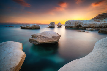 Beautiful sunset at the rocky beach near Limassol Cyprus with smooth water and white rocks standing out of water