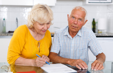 Smiling mature couple  in home interior filling up documents