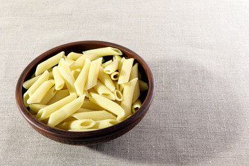 Pasta. Penne in a clay plate on a linen background.