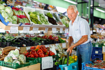 Obraz premium Satisfied elderly man with basket filled with fresh fruits and vegetables