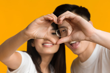Asian couple showing love sign over orange background