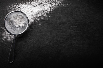 Powdered sugar scattered on a black stone countertop with a sifter for sifting , top view. - Powered by Adobe
