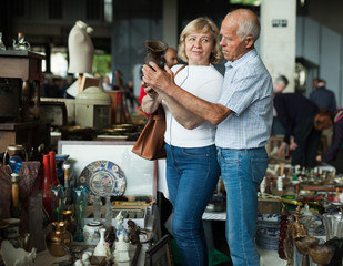 Smiling mature spouses buying retro handicrafts on flea market