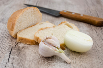 long loaf, onion, garlic and knife on a wooden table.