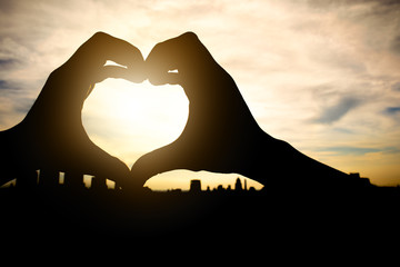 Woman making  heart with hands in sunset