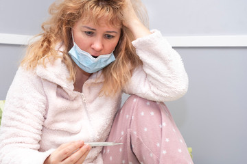  A European woman, has a virus and a cold, is sitting in a medical mask. The girl holds a...