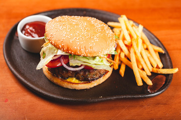 Fast food. Homemade hamburger and french fries on black plate.