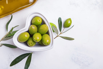 Heart shaped bowl full of green olives on a white table,