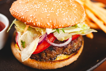 Fast food. Homemade hamburger and french fries on black plate.