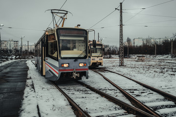 Modern tram in winter city in evening. Contemporary tram is on tram station in cloudy day in countryside.