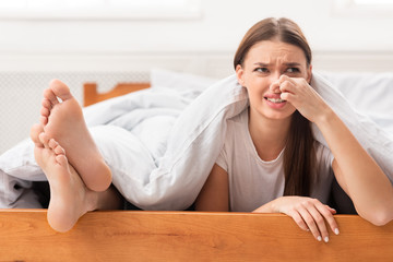 Woman Lying Near Boyfriend's Feet Pinching Nose In Bed Indoor