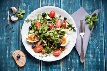 Salad of arugula, tomatoes, nuts and eggs. View from above. Wooden table. Place for text.