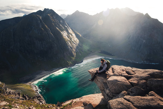 Famous view over Kvalvika beach from Ryten mountain. On of the best hikes in Lofoten islands in Norway. Girl sitting the edge of mountain with a view over ocean and beach and mountains
