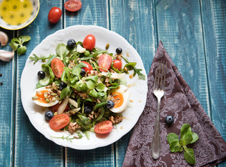 Salad of arugula, tomatoes, nuts and eggs. View from above. Wooden table. Place for text.