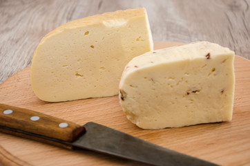two pieces of hard cheese on a wooden background and a knife. Ukrainian cheese.