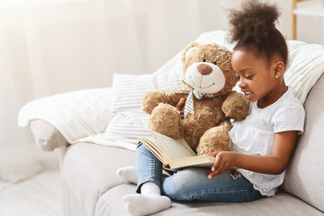 Black little girl reading fairy tale to her teddy bear
