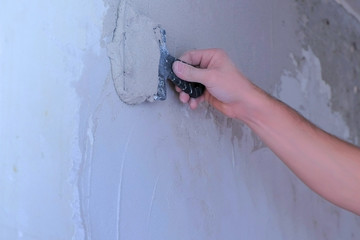 Plasterer man is spackling wall with putty plaster aligning wall, hand closeup. Finishing construction renovation works. Worker builder making overhaul in flat applying plaster on wall using trowel.