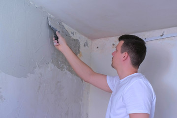 Plasterer man spackling wall with putty plaster aligning wall with spatula. Finishing construction...