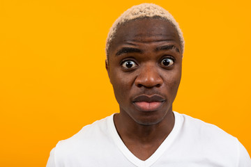 portrait of a blond surprised charismatic african man in a white t-shirt on a yellow studio background