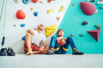 Father and teenage son sitting near the indoor climbing wall. They resting after the active...