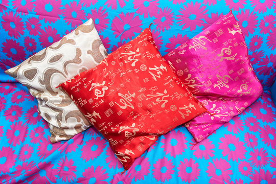 Three small size colorful pillows laying on a sofa, blue colored with pink floral patterns