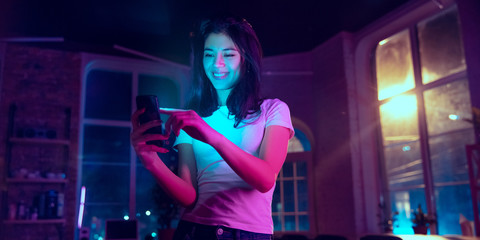 Taking selfie, vlog. Cinematic portrait of handsome stylish woman in neon lighted interior. Toned...