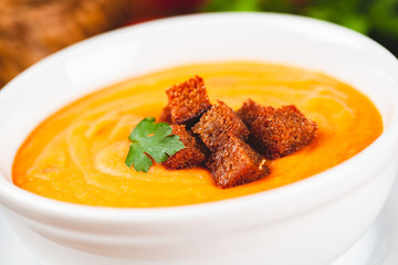 Vegetarian autumn pumpkin cream soup served in a white bowl with croutons.