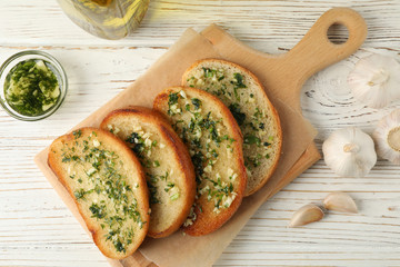 Board with garlic bread on white wooden background, top view