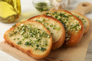 Board with toasted garlic bread and oil on wooden background, close up