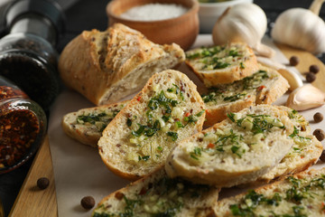 Board with toasted garlic bread and spices on wooden background, close up