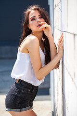 Pretty young brunette model in white summer blouse and jeans, summer street outdoors