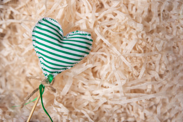 A heart sewn from green fabric lies on artificial straw. DIY made.