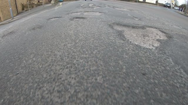 Vehicle driving over a damaged road which is covered in Potholes in the street. 