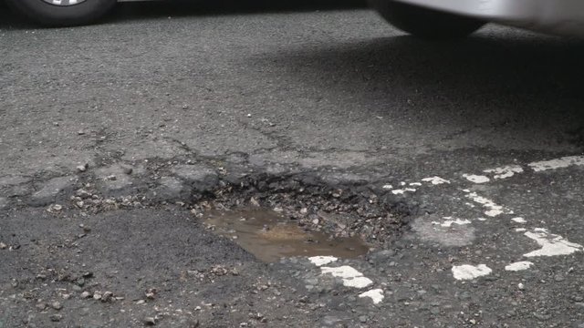 Vehicle driving over a damaged road with a Pothole in the street. Side View